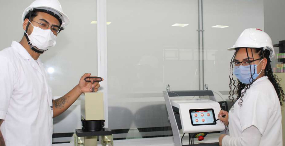 Dos estudiantes con casco y mascarilla manipulan dispositivos tecnológicos en un laboratorio escolar.